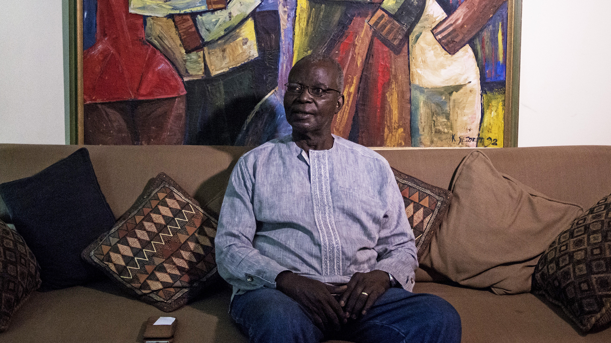 Mr. Dei sitting in his living room and in front of one of his favourite African painting. Accra, Ghana. 9th March 2017. PAINTING: The Wedding Party (1992) by Kofi Setordji (C) Jordi Perdigó