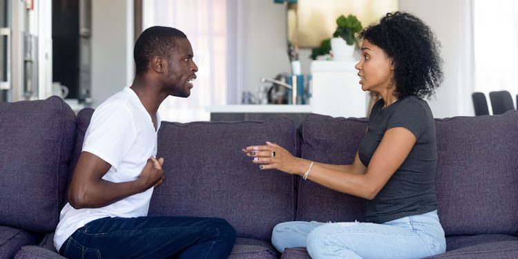 Unhappy African American couple quarreling, sitting on sofa at home, upset woman shouting, blaming black man, emotionally arguing, family conflict between wife and husband, break up