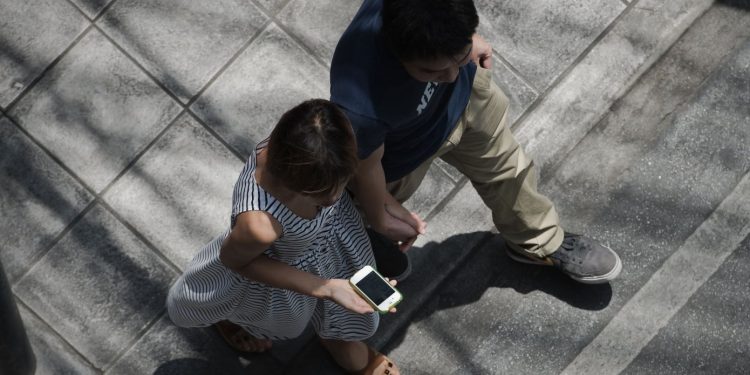 This picture taken on March 20, 2013 shows a woman holding her smartphone while walking with her partner in a street in Bangkok. A recent Facebook-sponsored study showed smartphone owners are often connected all day. People can be found glued to their smartphones at airports, on trains, in restaurants and even while walking on the street, creating a disconnection from their immediate surroundings. Smartphone sales are expected to continue to surge in 2013 with some 918 million units to be bought worldwide. AFP PHOTO / Nicolas ASFOURI (Photo by Nicolas ASFOURI / AFP) (Photo by NICOLAS ASFOURI/AFP via Getty Images)