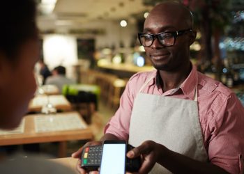 Modern customer holding her smartphone over payment terminal held by waiter