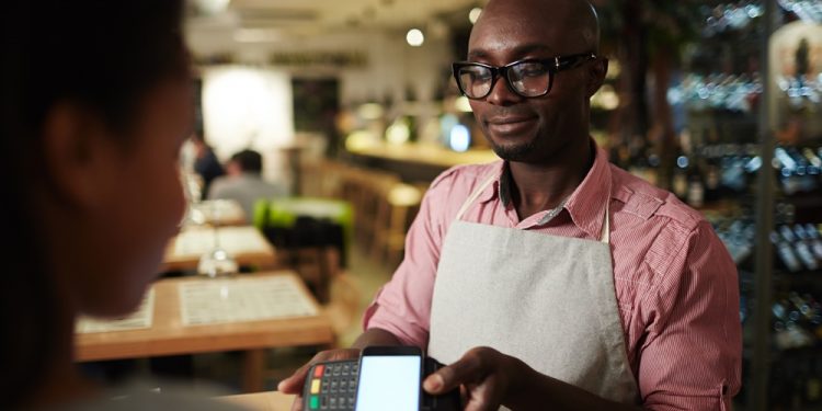 Modern customer holding her smartphone over payment terminal held by waiter